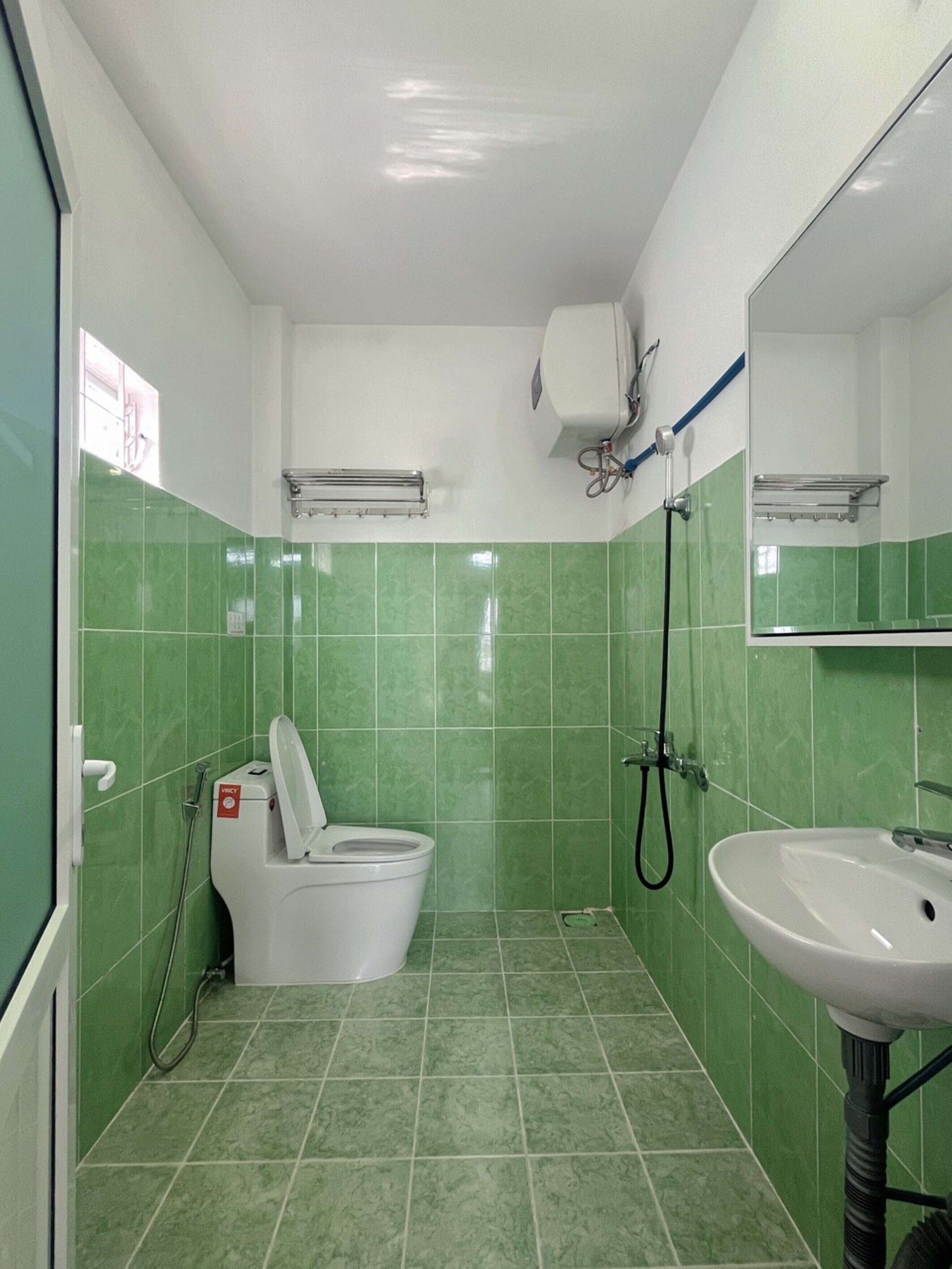 A bathroom with green tiles, a toilet, a sink, and a mirror.