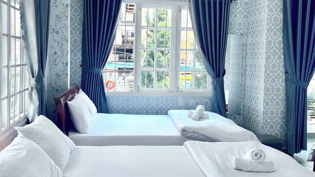 Una habitación de hotel con un ventanal grande, dos camas con sábanas blancas y cortinas azules.