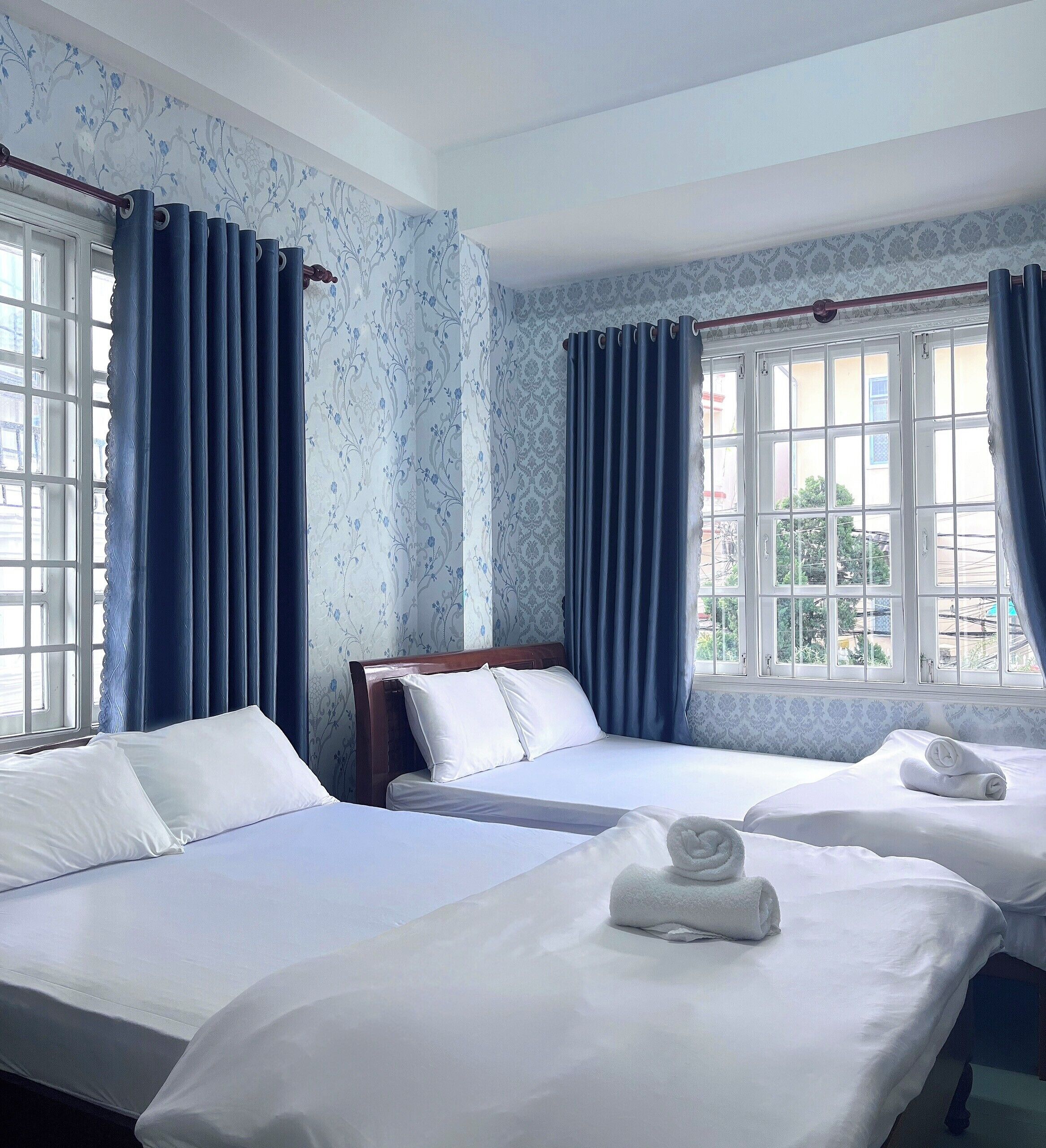A hotel room with two beds, a wooden headboard, and a window with blue curtains.