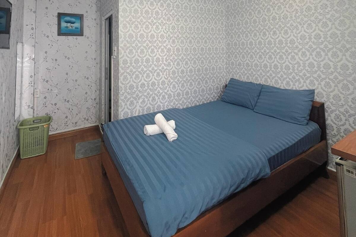 A bedroom with a single bed, a wooden floor, patterned wallpaper, and a small green basket.