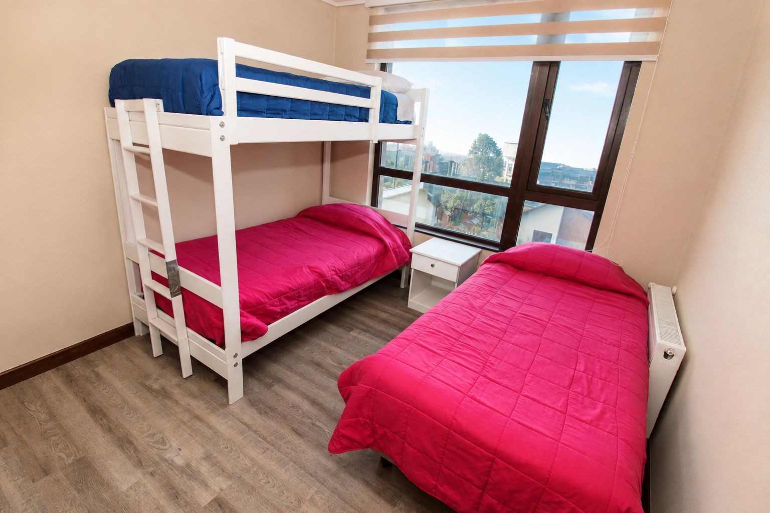 A room with two bunk beds, a window with blinds, and a white radiator.