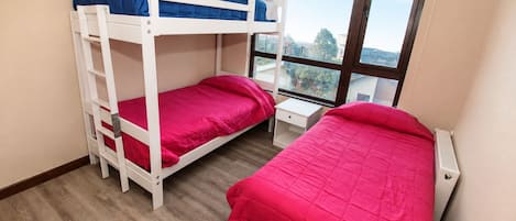 A room with two bunk beds, a window with blinds, and a white radiator.