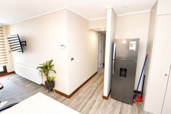 A modern kitchen with a refrigerator, a potted plant, and a flat-screen TV mounted on the wall.