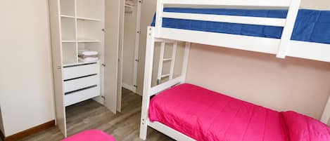A bunk bed with a pink mattress and a white frame, a white wardrobe with multiple compartments, and a wooden floor.