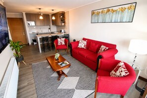 A modern living room with a red sofa, a wooden coffee table, and a kitchen in the background.