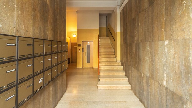 A hallway with a row of metal lockers on one side and a staircase on the other. - HouSmart Cimabue 1 (Bologna)