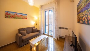 A living room with a sofa, a glass coffee table, a TV, and a painting on the wall. - HouSmart Cimabue 1 (Bologna)