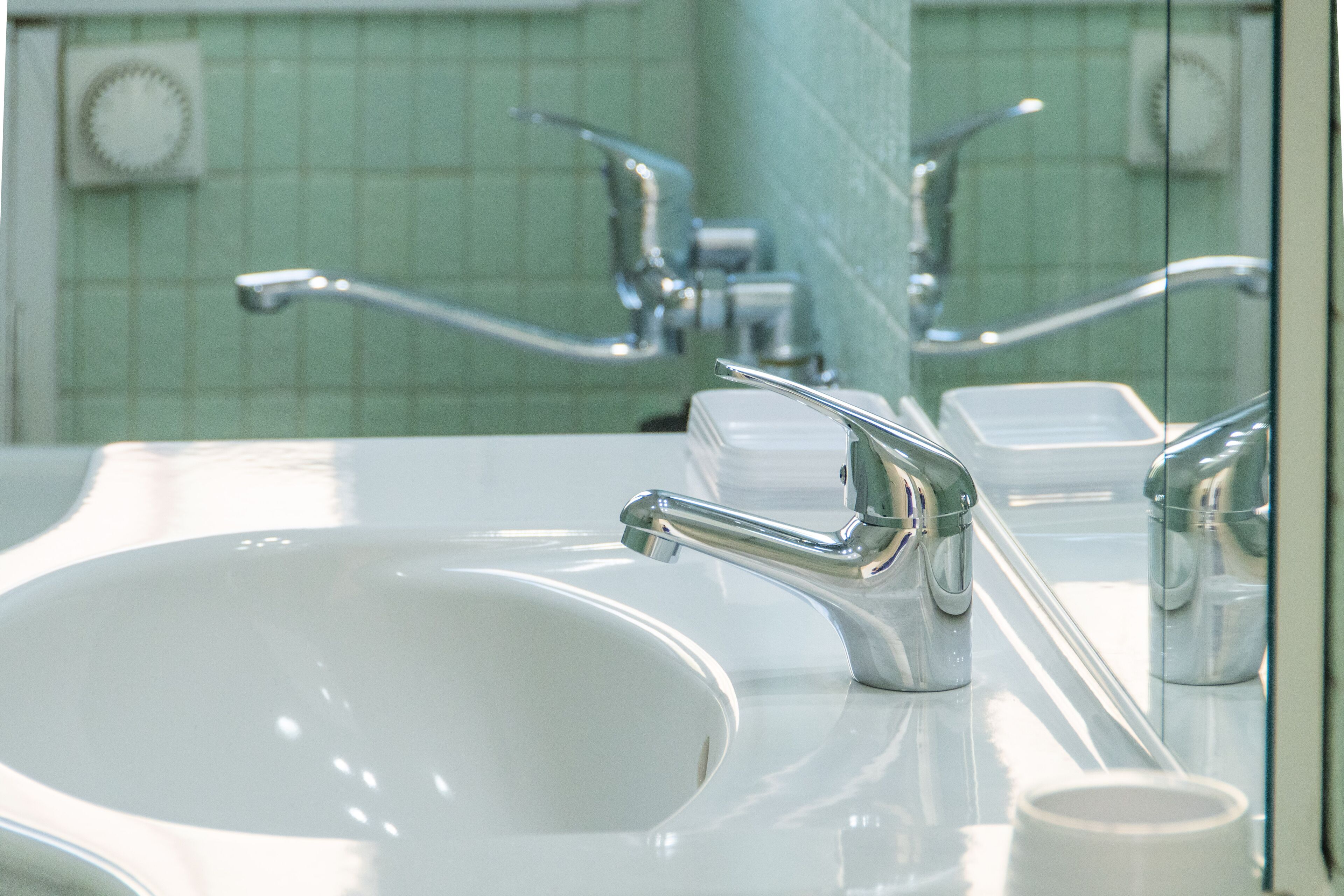 Une salle de bain avec un lavabo blanc, des robinets chromés et un miroir qui reflète le lavabo et les robinets.