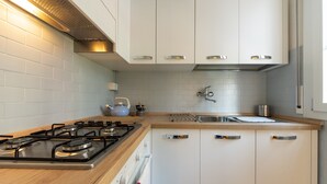 A modern kitchen with white cabinets, a wooden countertop, a gas stove, a kettle, and a sink. - HouSmart Cimabue 1 (Bologna)