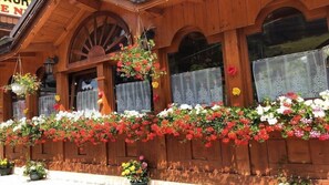 A wooden building with flower boxes and hanging flower baskets. - Logis Hotel la Boule de Neige (Samoëns)