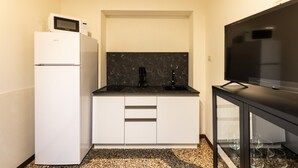A compact kitchenette with a white refrigerator, a microwave, a black marble backsplash, and a flat-screen TV on a black stand. - Afrodite Apartment With Jacuzzi by Wonderful Italy (Bologna)