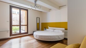 A bedroom with a round bed, a yellow accent wall, and a large window with a view of greenery. - Afrodite Apartment With Jacuzzi by Wonderful Italy (Bologna)