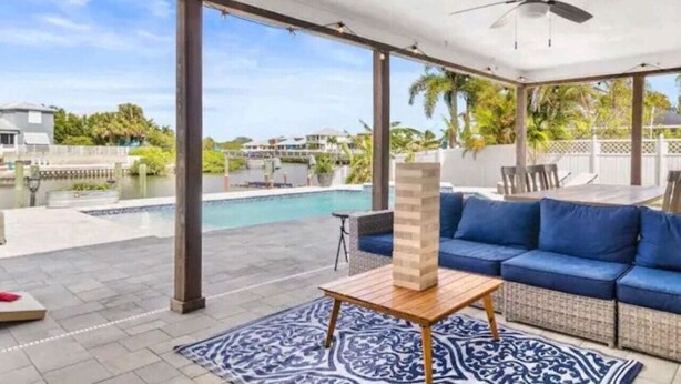 Un espacio exterior techado con piscina, asientos acolchados azules y una mesa de madera.
