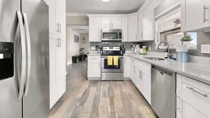 Una cocina moderna con electrodomésticos de acero inoxidable, armarios blancos y piso de madera.