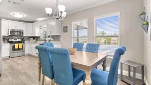 Una cocina moderna con armarios blancos, un horno de acero inoxidable y una zona de comedor con una mesa de madera y sillas tapizadas en azul.