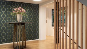 Een modern interieur met een behang, een houten vloer, een ronde tafel met een bloevas en een trap met houten leuningen.