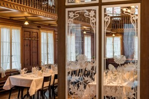 Comedor con mesas dispuestas para una comida, paneles de madera y ventanas grandes.