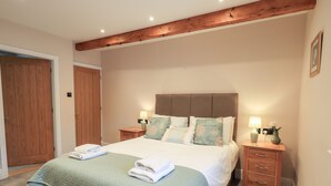 A bedroom with a large bed, wooden headboard, two bedside tables with lamps, and a wooden door. - Bottle Tops (Windermere)