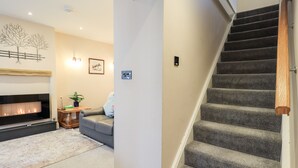 A living room with a fireplace, a sofa, a staircase, and a wall-mounted light fixture. - Bottle Tops (Windermere)