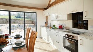 Una cocina moderna con armarios blancos, horno integrado y comedor con mesa y sillas de madera.
