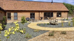 Una cabaña de madera con techo de tejas, un patio con mobiliario exterior y un jardín ajardinado.