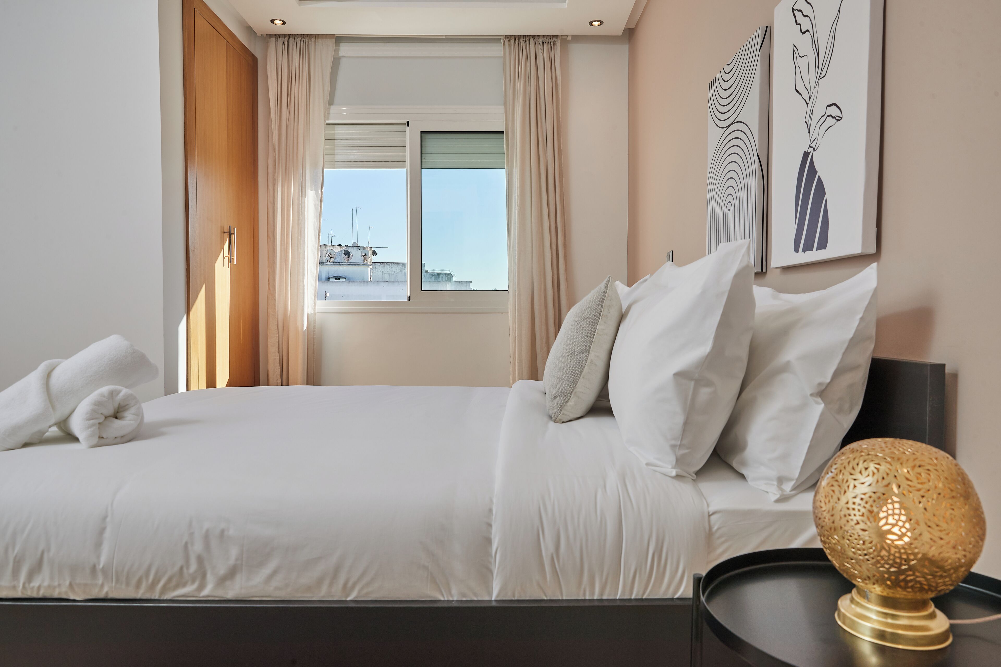 A neatly made bed with white linens and pillows, a bedside lamp, and artwork on the wall.