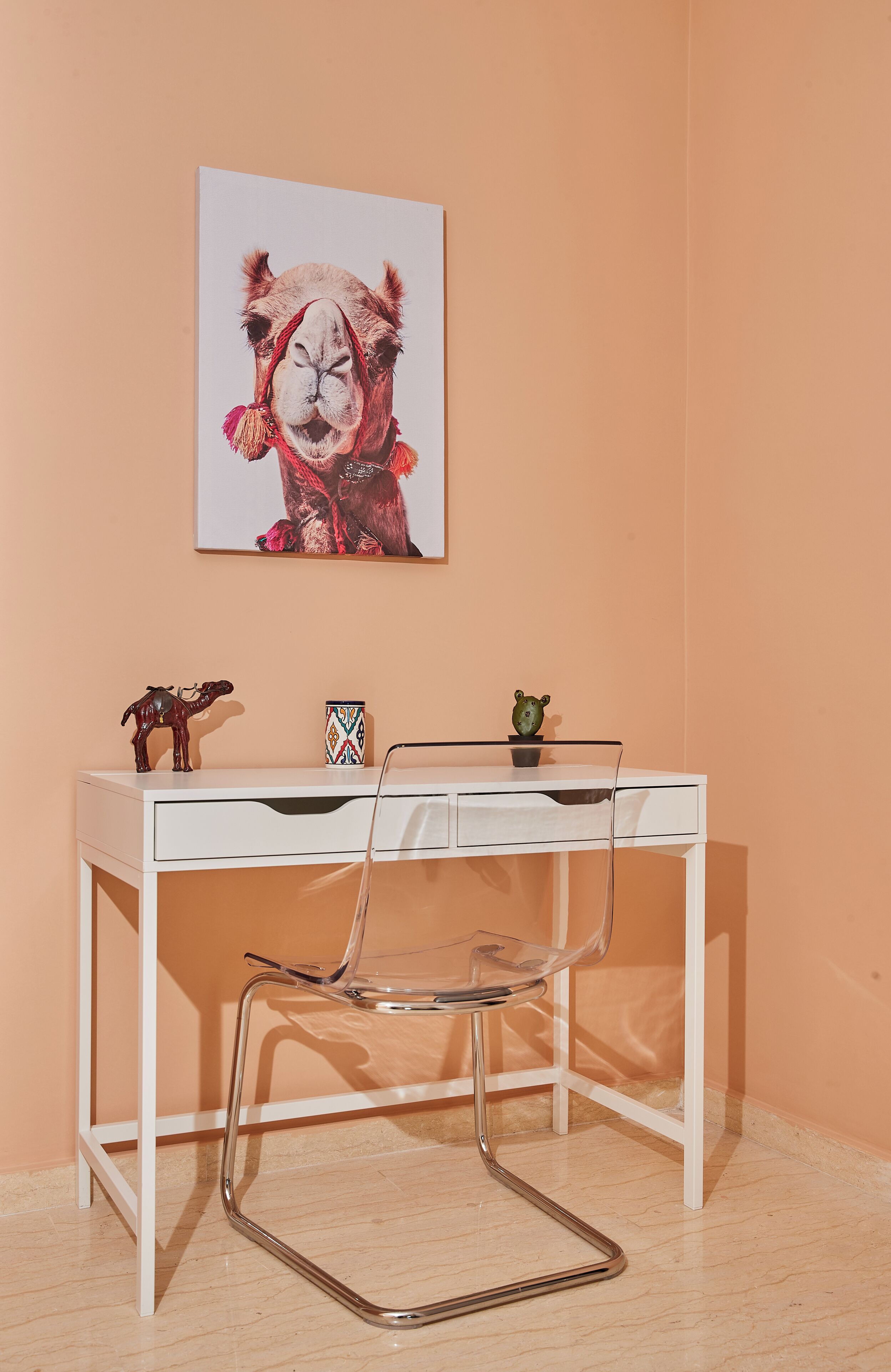 A desk with a clear chair, a framed picture on the wall, and a cactus on the desk.
