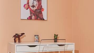 A desk with a clear chair, a framed picture on the wall, and a cactus on the desk.