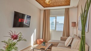 A modern living room with a flat-screen TV mounted on the wall, a sofa, a coffee table, and a large window with curtains. - StayHere Rabat - Hassan Heritage (Rabat)