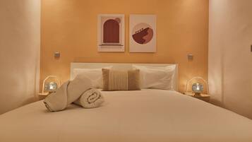 A neatly made bed with a rolled towel, two wall-mounted artworks, and bedside lamps.