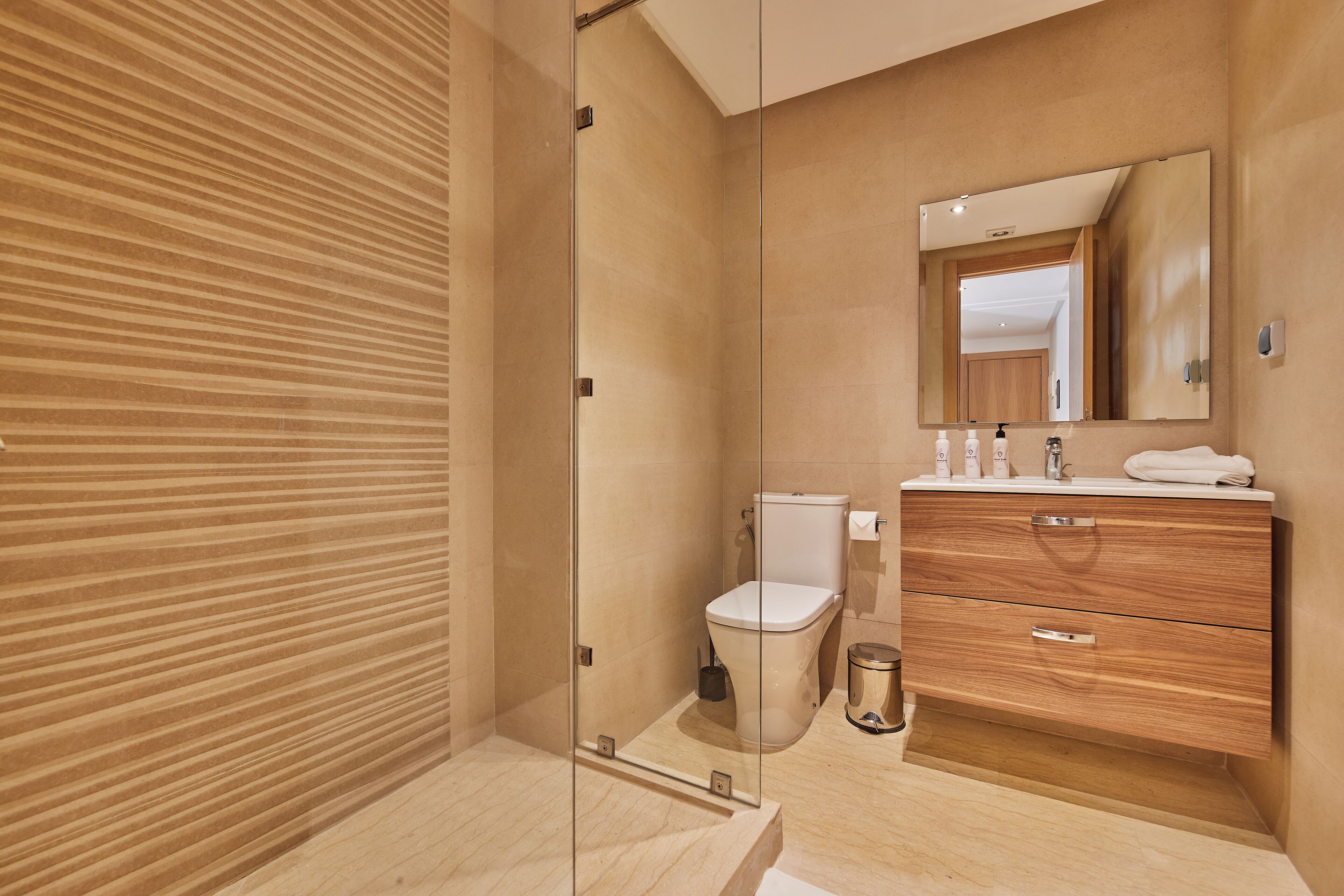 A modern bathroom with a glass-enclosed shower, a wooden vanity, and a large mirror.