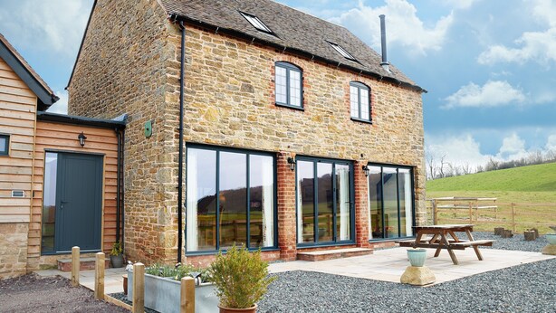 A stone building with large windows, a wooden door, and a picnic table in the front. - A beautiful barn conversion sleeping four guests. (Acton Burnell, Shrewsbury)