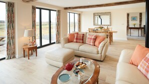 A spacious living room with a sofa, a coffee table with snacks, and a dining area in the background. - A beautiful barn conversion sleeping four guests. (Acton Burnell, Shrewsbury)