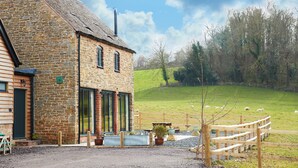A stone building with a sloped roof, a wooden fence, and a grassy field with sheep. - A beautiful barn conversion sleeping four guests. (Acton Burnell, Shrewsbury)