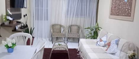 Una sala de estar con un sofá, dos sillones, una mesa de comedor y un televisor.