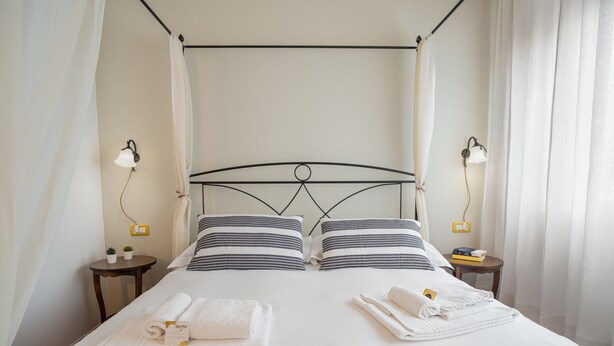 A bed with a black metal frame, white bedding, two bedside tables with lamps, and a small table with plants. - B&B Antica Posta (Florence)