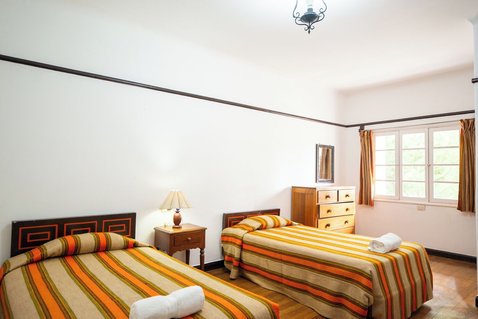 A bedroom with two beds, a nightstand, a dresser, and a window with curtains.