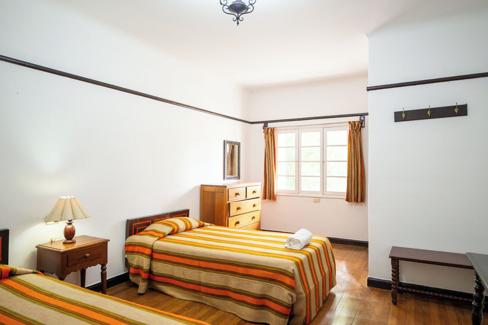 A bedroom with a bed, a nightstand, a dresser, a window with curtains, and a small table.