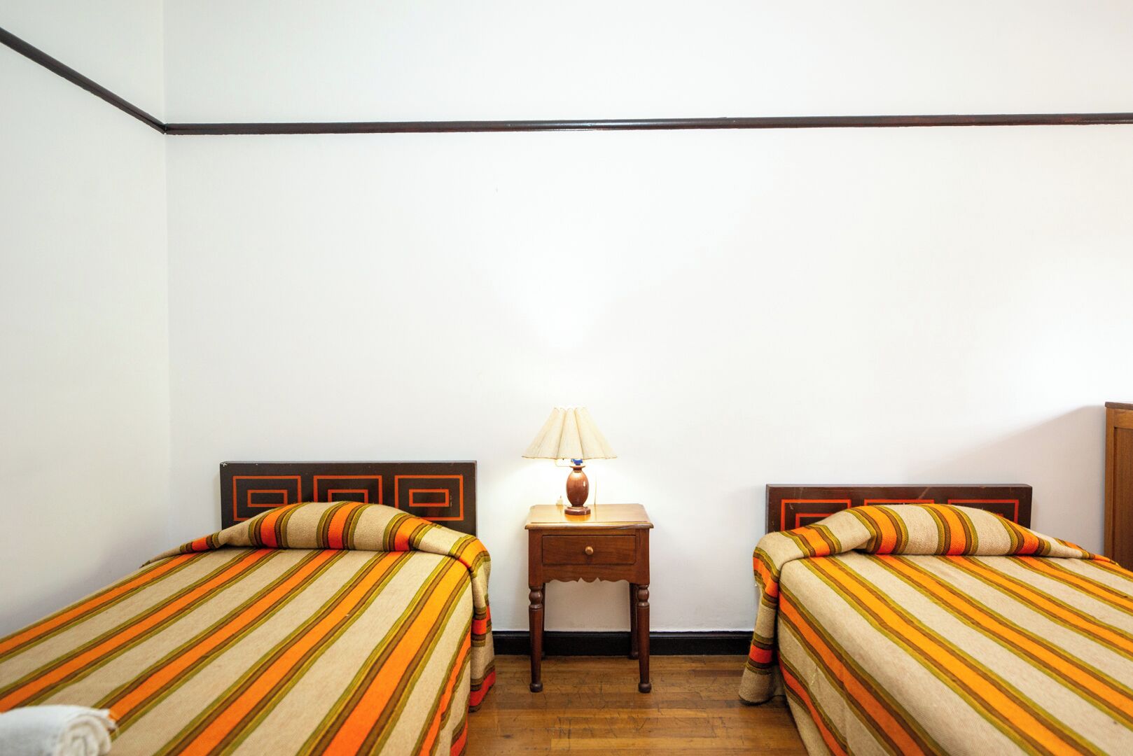 A room with two beds, a nightstand, and a lamp.