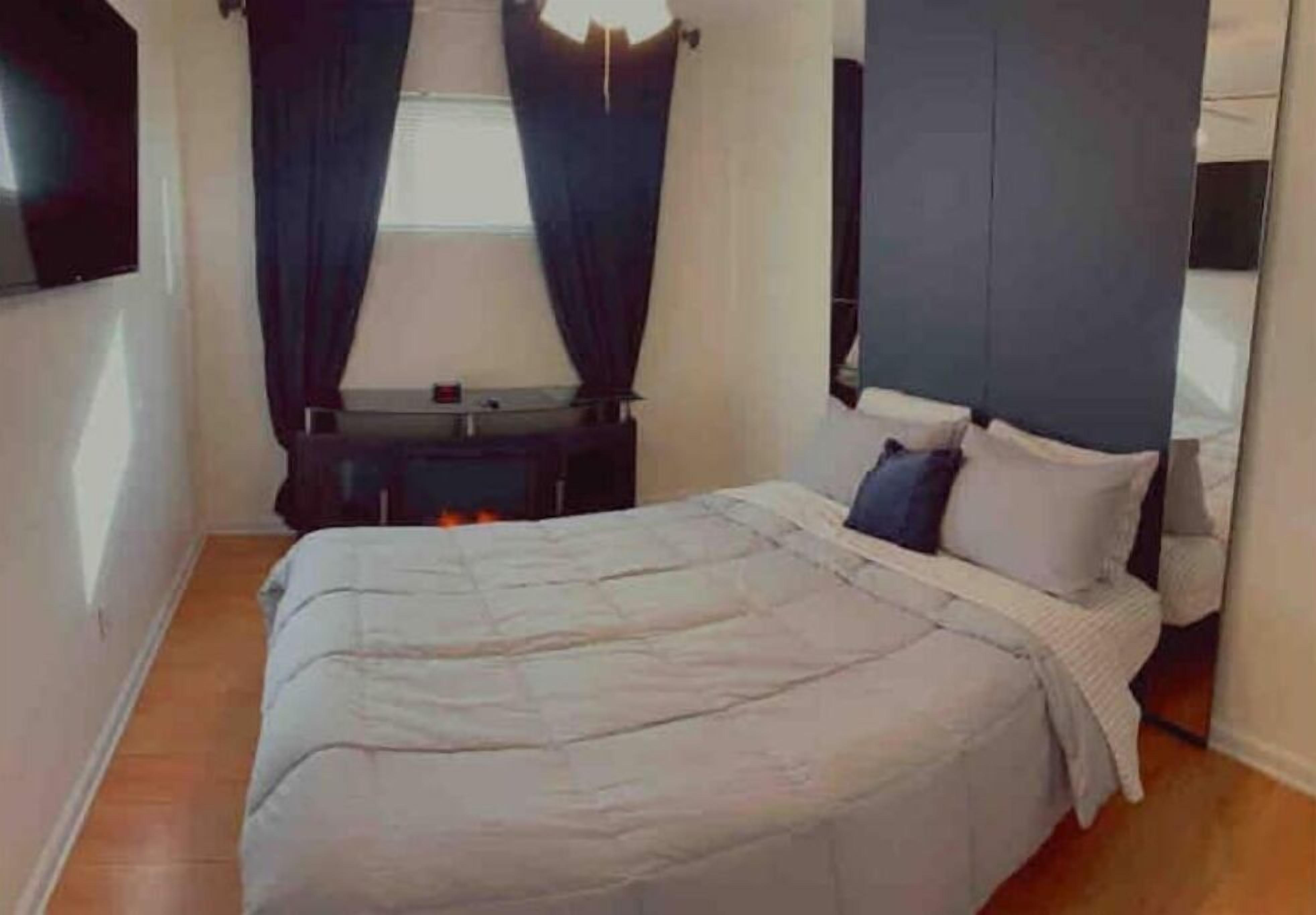 A bedroom with a bed, a nightstand, a lamp, and a window with curtains.