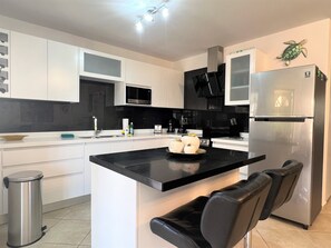 A modern kitchen with white cabinets, a black countertop, and a stainless steel refrigerator.