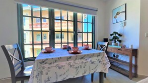 A dining area with a table set for four, a wooden sideboard, and a window with a view of buildings. - Sea Turtle Condo 2 Bdr-2 Bth in Palm Beach Area, walking distance to the beach. (Noord)