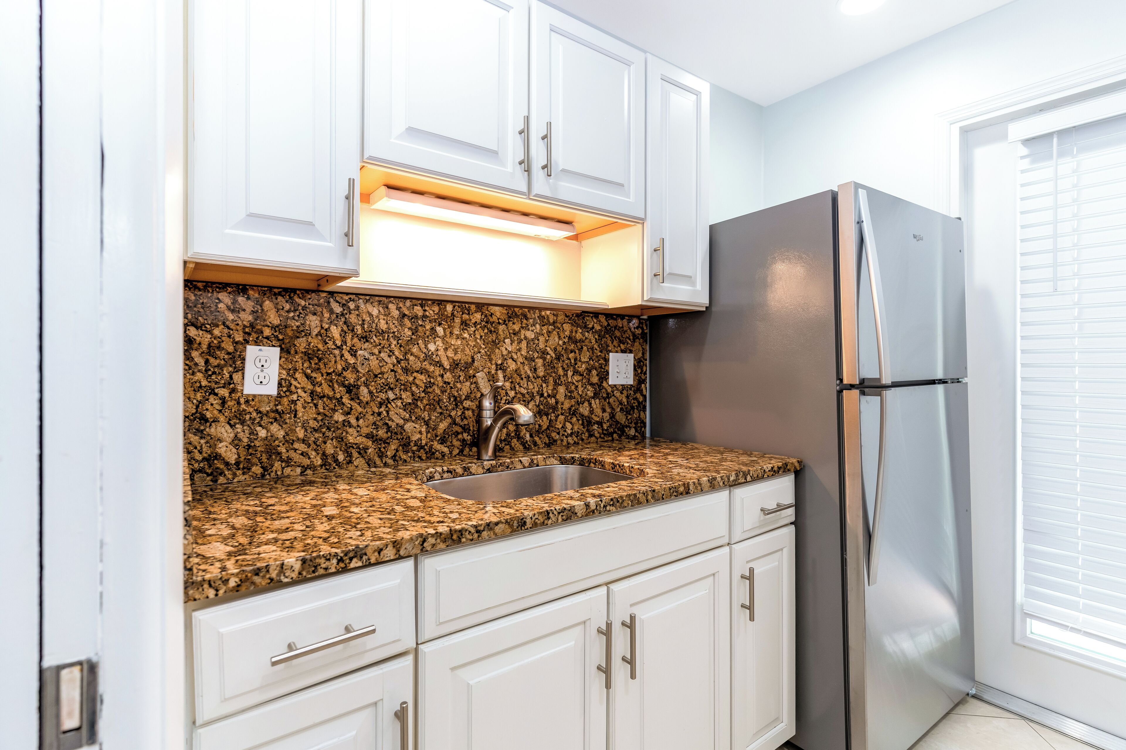 A kitchen with white cabinets, a granite countertop, a stainless steel refrigerator, and a built-in sink.