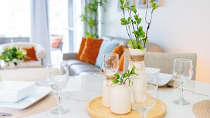 A dining table set with white plates, cutlery, and glasses, with a vase of green plants and candles on a wooden board.