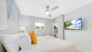 A bedroom with a bed, a ceiling fan, a TV on the wall, and a window with curtains.