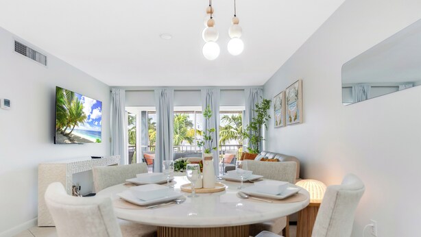 A modern dining area with a round table, white chairs, and a view of the outdoors through large windows.