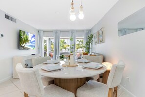 A modern dining area with a round table, white chairs, and a view of the outdoors through large windows.