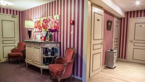 A room with striped wallpaper, a red armchair, a wooden cabinet, and a small table. - Le Cottage Hotel (Bruay-la-Buissiere)