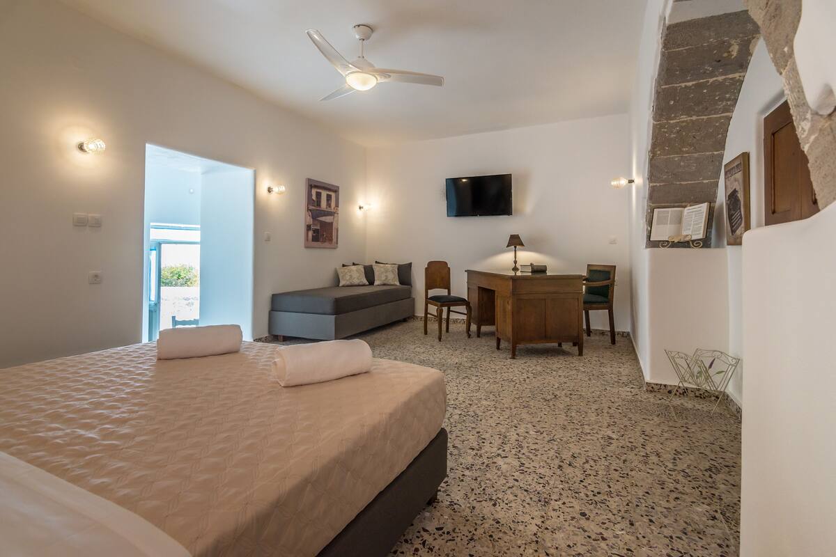 A bedroom with a bed, a desk, a chair, a television, and a ceiling fan.