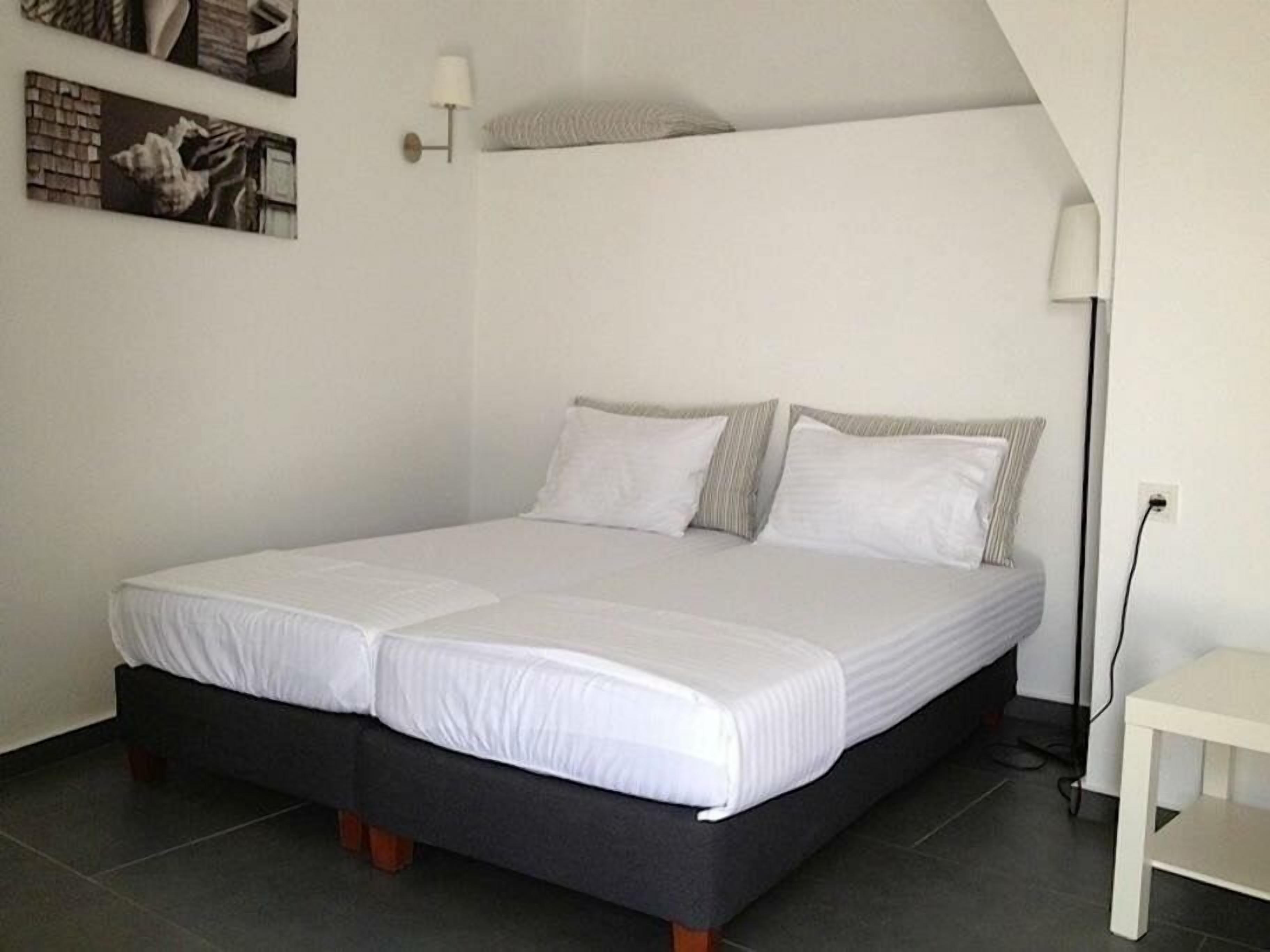 A bed with white bedding, a small bedside table, and a lamp on the wall.